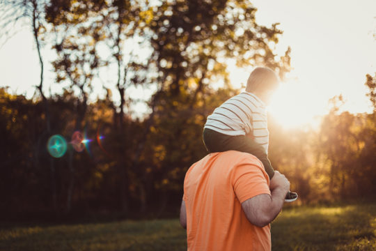 Dad holding son on shoulders in sunlight, highlighting the Canadian childcare benefit