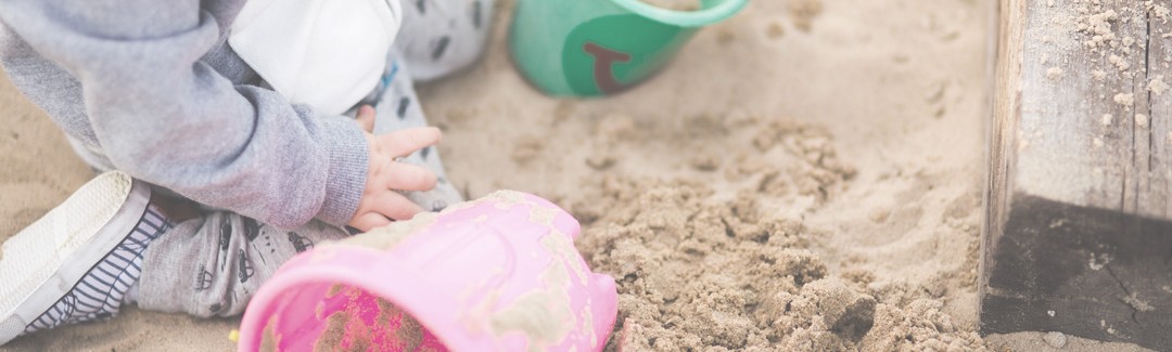 Child in a sandbox with buckets and sand; highlighting in home daycare taxes