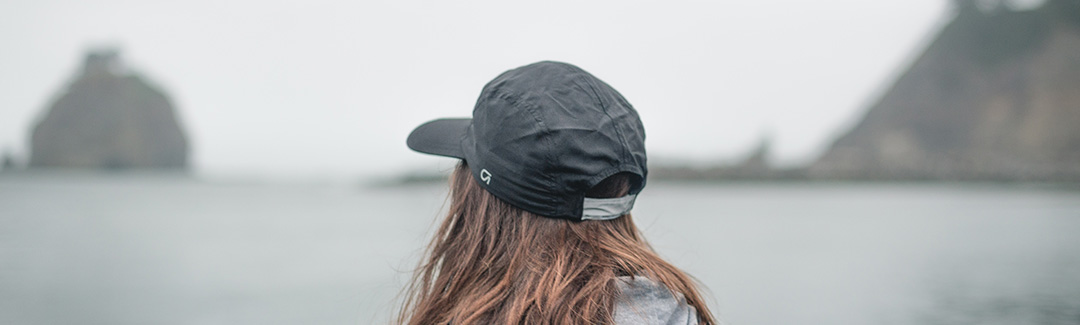 Pensive woman in black hat overlooking water at the beach on a gray day; highlighting corporation loans