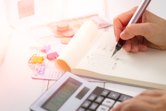 Man writing numbers on a notepad with a calculator highlighting proposed tax changes